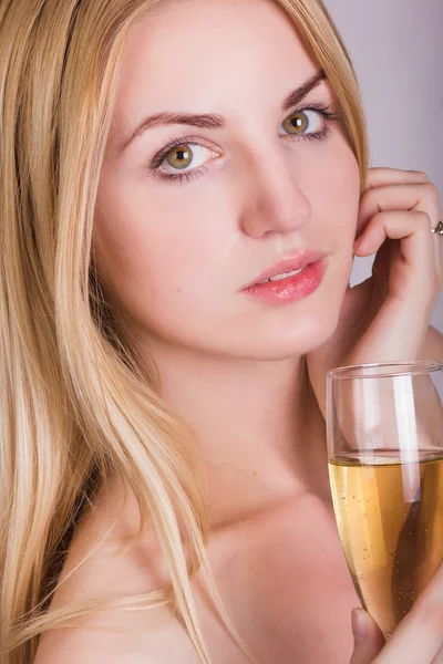 Portrait of a beautiful young blonde woman on a white background in a short white dress with black lace. Cute girl posing with a glass of champagne in her hands. — Stock Photo, Image