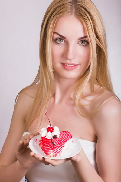 Portrait of a beautiful young blonde woman in the studio on a white background. Girl posing in a beautiful dress with a cake in the shape of heart. — Stock Photo, Image