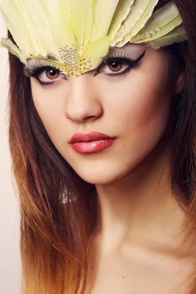 Portrait d'une belle jeune femme aux cheveux bruns aux cheveux longs dans un studio. Maquillage avec une longue flèche noire et des plumes longues jaunes — Photo