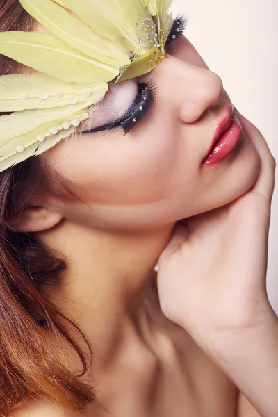 Portrait d'une belle jeune femme aux cheveux bruns aux cheveux longs dans un studio. Maquillage avec une longue flèche noire et des plumes longues jaunes — Photo