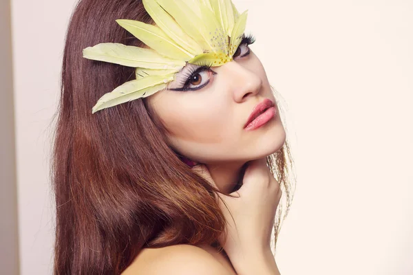 Retrato de bela jovem mulher de cabelos castanhos com cabelo comprido em um estúdio. Maquiagem com seta preta longa e penas longas amarelas — Fotografia de Stock