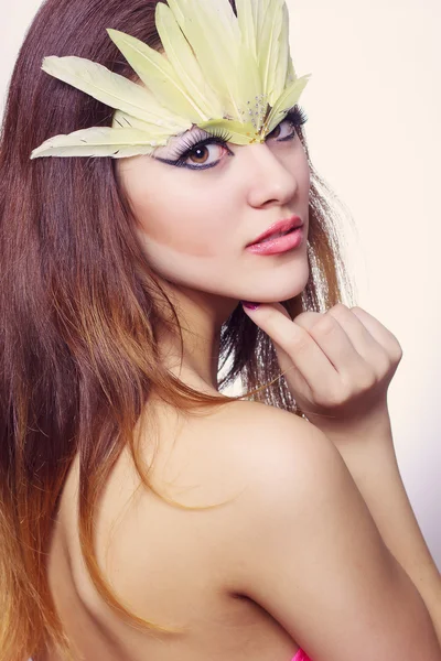 Portrét krásné mladé hnědovlasá žena s dlouhými vlasy v ateliéru. make-up s dlouhou černou šipkou a žluté dlouhé peří — Stock fotografie