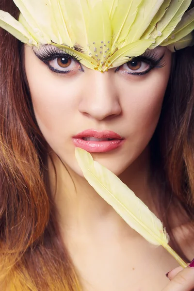 Portrait d'une belle jeune femme aux cheveux bruns aux cheveux longs dans un studio. Maquillage avec une longue flèche noire et des plumes longues jaunes — Photo