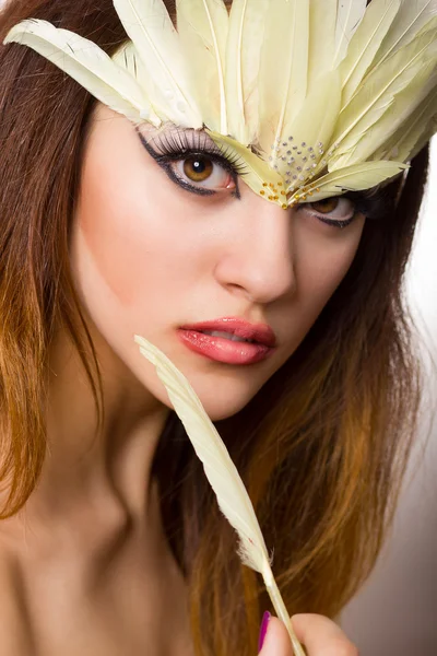 Portrait d'une belle jeune femme aux cheveux bruns aux cheveux longs dans un studio. Maquillage avec une longue flèche noire et des plumes longues jaunes — Photo