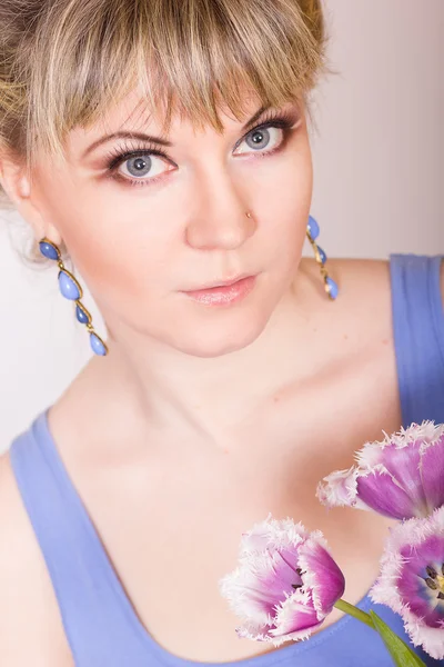 Retrato de uma bela jovem loira em um fundo branco em um vestido azul. Mulher posando com um buquê de tulipas roxas . — Fotografia de Stock