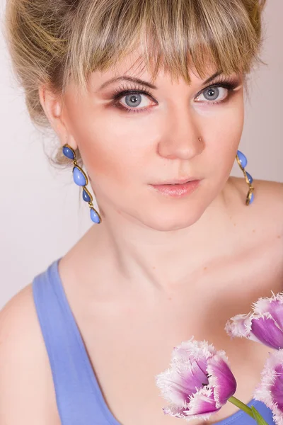 Retrato de una hermosa joven rubia sobre un fondo blanco en un vestido azul. Mujer posando con un ramo de tulipanes morados . —  Fotos de Stock