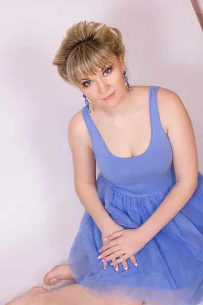 Porträtt av en vacker ung blond kvinna med kort hår och klädd i en blå kort klänning. flicka poserar med olika känslor i studion. — Stockfoto