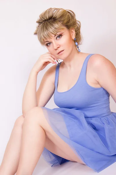 Portret van een mooie jonge blonde vrouw met kort haar en gekleed in een blauwe korte jurk. meisje poseren met verschillende emoties in de studio. — Stockfoto