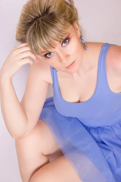 Portrait of a beautiful young blonde woman with short hair and dressed in a blue short dress. Girl posing with different emotions in the studio. — Stock Photo, Image