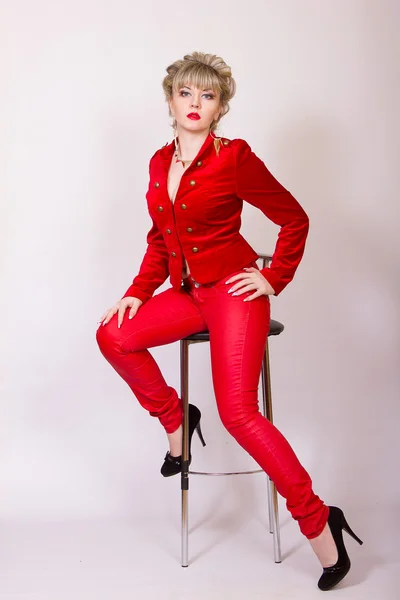 Porträtt av en vacker ung blond flicka med kort hår i en sexig business-stil. en kvinna klädd i en röd jacka och röda byxor. — Stockfoto