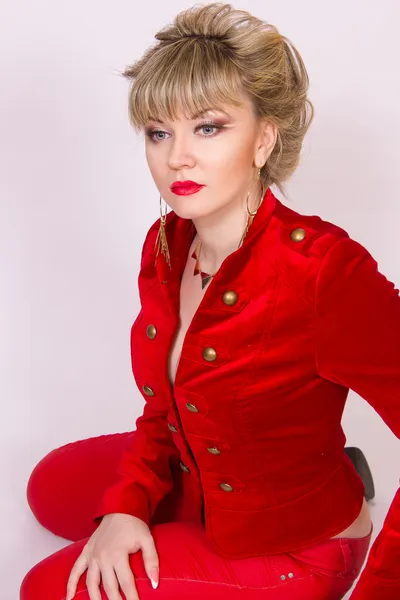 Porträtt av en vacker ung blond flicka med kort hår i en sexig business-stil. en kvinna klädd i en röd jacka och röda byxor. — Stockfoto