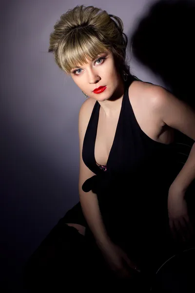 Porträt einer schönen jungen blonden Frau, die mit hellem Make-up kocht. Mädchen in schwarzem Abendkleid auf schwarzem Hintergrund. — Stockfoto