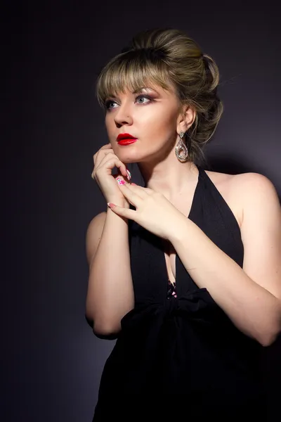 Portrait of a beautiful young blonde woman cooks with bright makeup. Girl dressed in black evening dress on a black background. — Stock Photo, Image