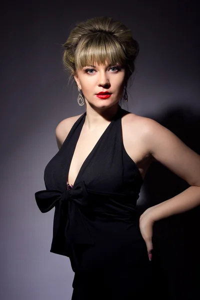 Portrait of a beautiful young blonde woman cooks with bright makeup. Girl dressed in black evening dress on a black background. — Stock Photo, Image