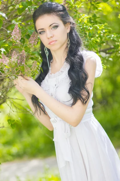 Όμορφη νεαρή μελαχρινή θέτουν στη φύση. κορίτσι με μαλλιά και μακιγιάζ σε λευκό ρομαντικό φόρεμα — Φωτογραφία Αρχείου
