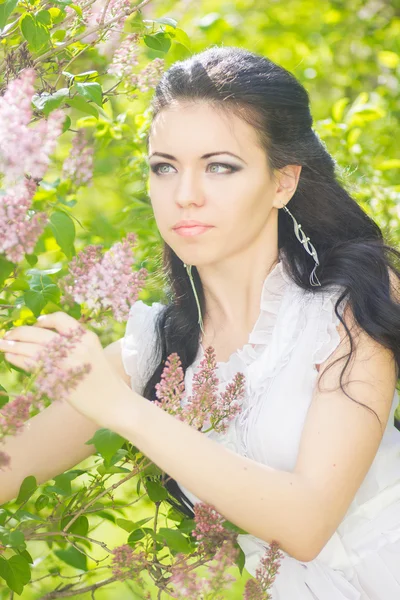 Vacker ung brunett poserar i naturen. flicka med hår och smink i vit romantisk klänning — Stockfoto