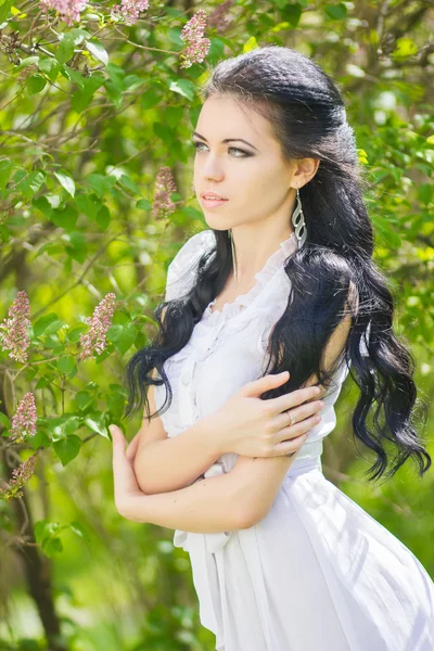 Hermosa joven morena posando en la naturaleza. Chica con pelo y maquillaje en vestido romántico blanco —  Fotos de Stock