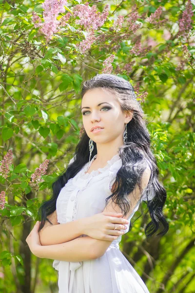 Hermosa joven morena posando en la naturaleza. Chica con pelo y maquillaje en vestido romántico blanco —  Fotos de Stock