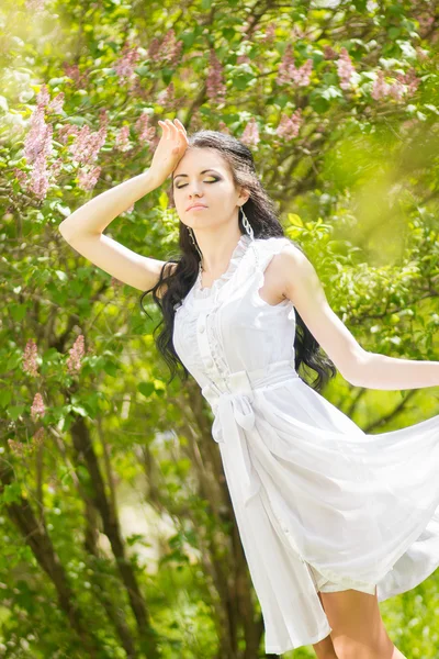 Hermosa joven morena posando en la naturaleza. Chica con pelo y maquillaje en vestido romántico blanco —  Fotos de Stock