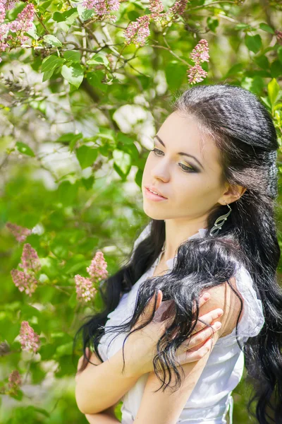 Hermosa joven morena posando en la naturaleza. Chica con pelo y maquillaje en vestido romántico blanco —  Fotos de Stock