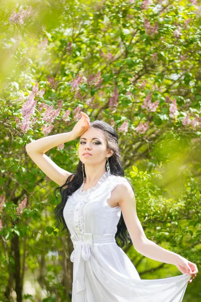 Hermosa joven morena posando en la naturaleza. Chica con pelo y maquillaje en vestido romántico blanco —  Fotos de Stock