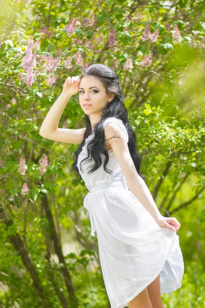 Linda jovem morena posando na natureza. Menina com cabelo e maquiagem em vestido romântico branco — Fotografia de Stock