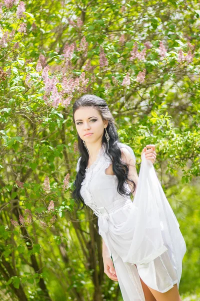 Linda jovem morena posando na natureza. Menina com cabelo e maquiagem em vestido romântico branco — Fotografia de Stock