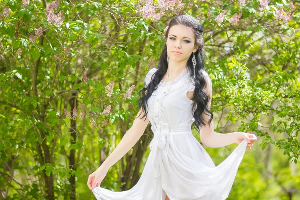 Schöne junge Brünette posiert in der Natur. Mädchen mit Haaren und Make-up im weißen romantischen Kleid — Stockfoto