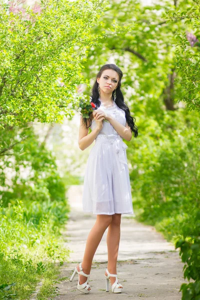 Vacker ung brunett poserar i naturen. flicka med hår och smink i vit romantisk klänning — Stockfoto