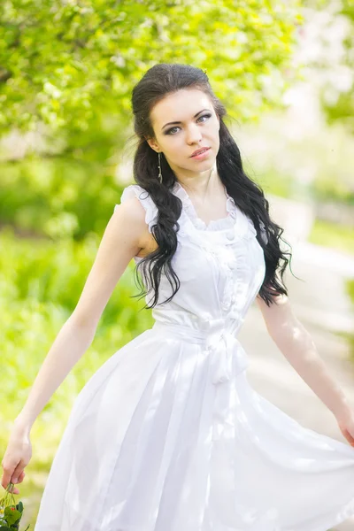 Hermosa joven morena posando en la naturaleza. Chica con pelo y maquillaje en vestido romántico blanco — Foto de Stock