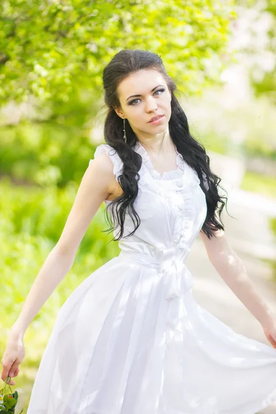 Bella giovane bruna in posa nella natura. Ragazza con capelli e trucco in abito romantico bianco — Foto Stock