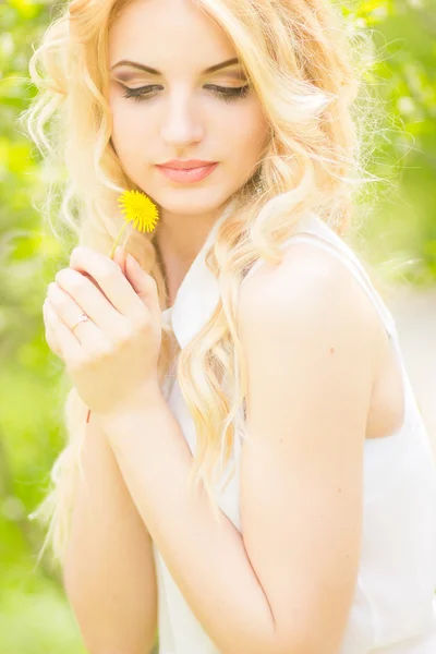 Portrait of a beautiful young blonde woman with dandelions. Girl posing in nature and smiling — Stock Photo, Image