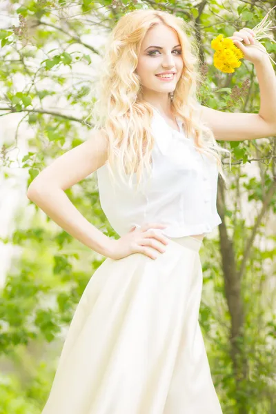 Retrato de una hermosa joven rubia con dientes de león. Chica posando en la naturaleza y sonriendo —  Fotos de Stock