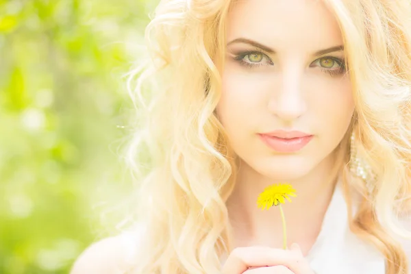 Retrato de una hermosa joven rubia con dientes de león. Chica posando en la naturaleza y sonriendo — Foto de Stock