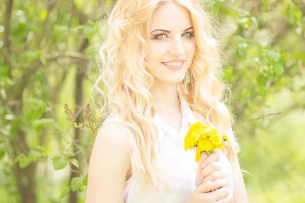 Retrato de una hermosa joven rubia con dientes de león. Chica posando en la naturaleza y sonriendo —  Fotos de Stock