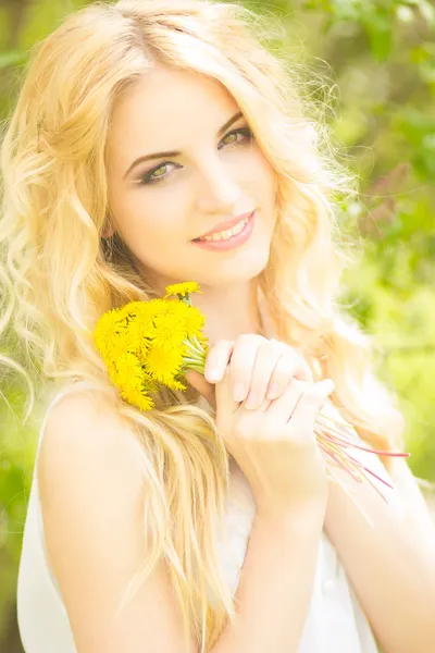 Retrato de una hermosa joven rubia con dientes de león. Chica posando en la naturaleza y sonriendo —  Fotos de Stock