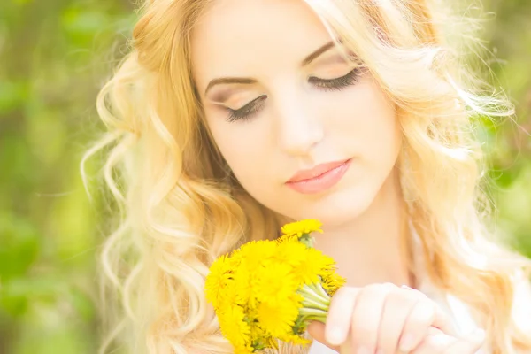Portrait of a beautiful young blonde woman with dandelions. Girl posing in nature and smiling — Stock Photo, Image