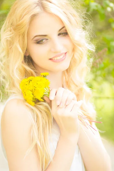 Retrato de una hermosa joven rubia con dientes de león. Chica posando en la naturaleza y sonriendo — Foto de Stock