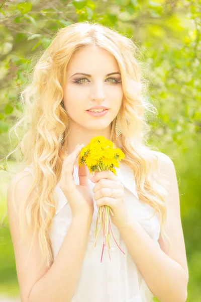 Portret pięknej młodej kobiety blondynka z mniszek. dziewczyna pozowanie w przyrodzie i uśmiechając się — Zdjęcie stockowe