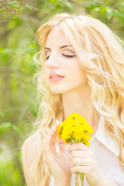 Portret van een mooie jonge blonde vrouw met paardebloemen. meisje poseren in de natuur en glimlachen — Stockfoto