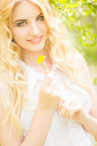 Retrato de una hermosa joven rubia con dientes de león. Chica posando en la naturaleza y sonriendo — Foto de Stock