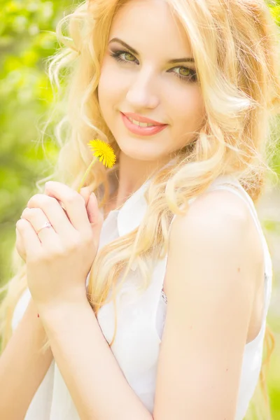 Retrato de una hermosa joven rubia con dientes de león. Chica posando en la naturaleza y sonriendo —  Fotos de Stock