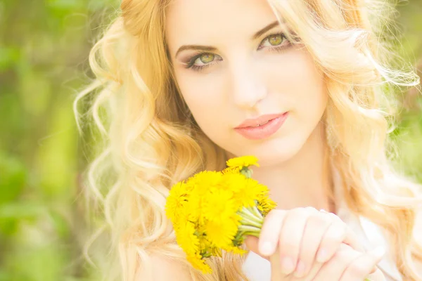 Porträt einer schönen jungen blonden Frau mit Löwenzahn. Mädchen posiert in der Natur und lächelt — Stockfoto