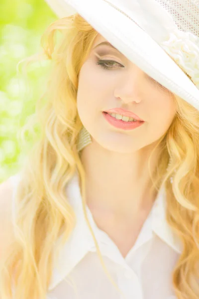 波浪形的头发，在大自然中一个美丽的年轻金发女子的画像。坐在公园的草地上戴的白帽子的女孩 — 图库照片