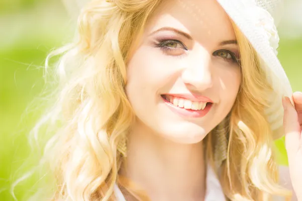 Portrait of a beautiful young blonde woman with wavy hair in nature. Girl in white hat sitting on the grass in the park — Stock Photo, Image