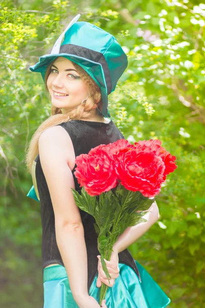 Portrait of a beautiful young woman in a costume of the Mad Hatter in nature. Girl posing with a bouquet of red peonies — Stock Photo, Image