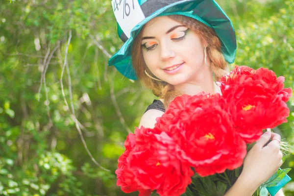 Porträtt av en vacker ung kvinna i en kostym av mad hatter i naturen. flicka som poserar med en bukett av röda pioner — Stockfoto
