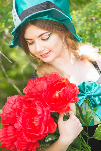 Portret van een mooie jonge vrouw in een kostuum van de mad hatter in de natuur. meisje poseren met een boeket van rode pioenrozen — Stockfoto