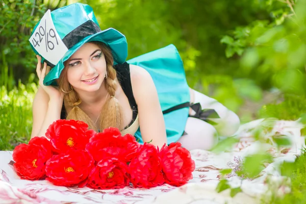 Porträt einer schönen jungen Frau im Kostüm des verrückten Hutmachers in der Natur. Mädchen posiert mit einem Strauß roter Pfingstrosen — Stockfoto