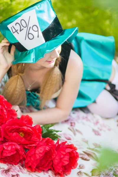 Portrait of a beautiful young woman in a costume of the Mad Hatter in nature. Girl posing with a bouquet of red peonies — Stock Photo, Image